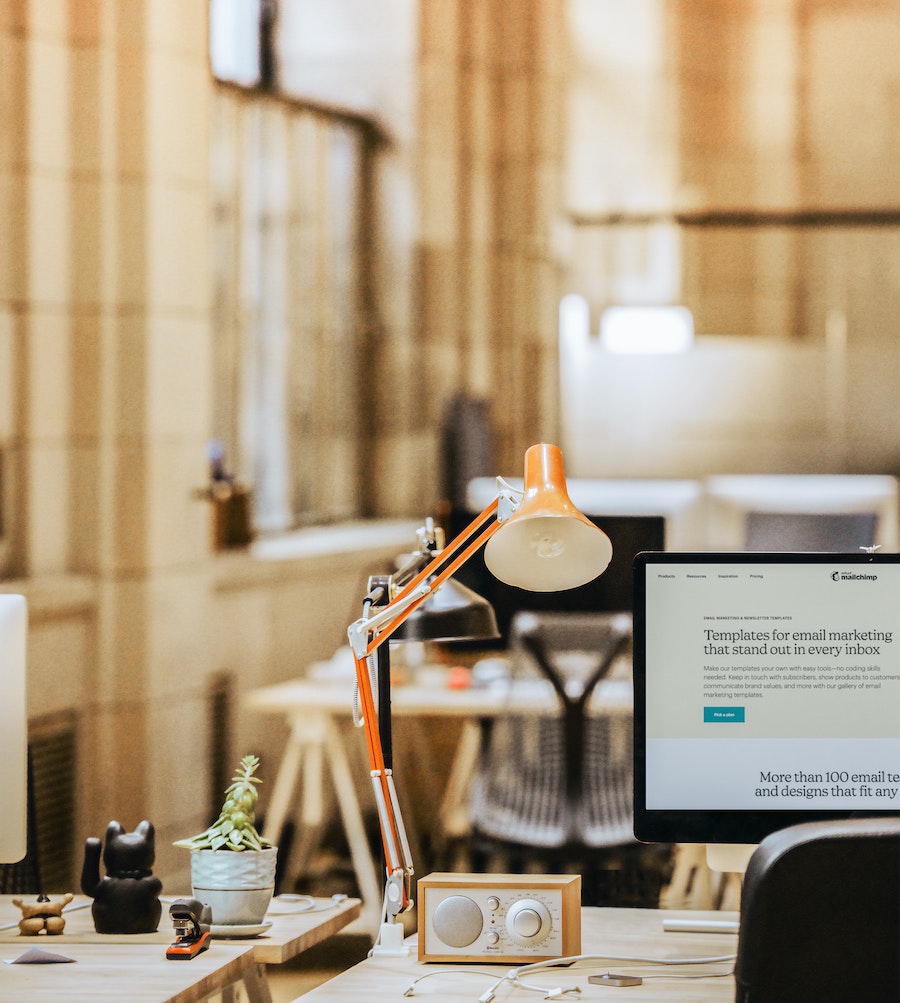 a scene from a coworking space with a table, tivoli radio, imac, and other accessories on the table including a lamp. a cozy ambiance.